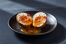 Load image into Gallery viewer, soy marinated soft yolk egg, with speckles of white seasme &amp; small cut chili, in a darker background and soft natural lighting to make it look delicious. Use a higher camera angle to showcase the soft yolk.
